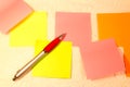 A ballpoint pen and blank sticky notes in orange, yellow and pink.