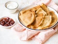 Several thin pancakes or crepes, folded four times on a white plate and strawberries jam and cream in bowls