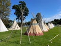 Several traditional teepees have been set up at a festival.Skeletal frame of wooden poles seen in the foreground.