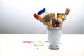 Several used paint brushes with different colors in a ceramic cup and color stains on the white table against a gray background, Royalty Free Stock Photo