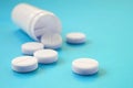 Several white tablets fall out of the plastic jar on the blue surface. Background image on medical and pharmaceutical topics