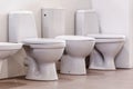 Several white toilet bowls stand in a row