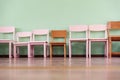 Several wooden children chairs of different sizes stand in row along empty wall