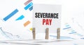 Severance pay text on paper sheet with chart, dice, spectacles, pen, laptop and blue and yellow push pin on wooden table -