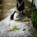 Older non recognisable woman sweeping up hailstones in courtyard after hailstone storm