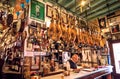 Older owner of tapas bar waiting for visitors inside retro decoration with traditional dry-cured ham legs