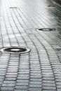 Sewer manhole on wet cobblestone street Royalty Free Stock Photo