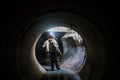 Sewer tunnel worker examines sewer system damage and wastewater leakage