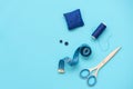 Sewing accessories with threads, scissors, pins, fabric, buttons and sewing tape on blue background. Top view. Flat lay