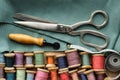 Sewing items: retro tailoring scissors, measuring tape, wooden spools of threads, cutting knife and green cloth. Top view