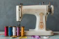 Sewing machine with colorful spools on a table against a grey background, with ribbon and thread in front of the in Royalty Free Stock Photo