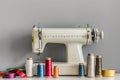 Sewing machine with colorful spools on a table against a grey background, with ribbon and thread in front of the in Royalty Free Stock Photo