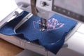 Sewing machine with embroidery unit stitches a light pink magnolia on boiled wool in trendy classic blue on