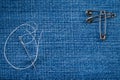 Sewing needle with a white thread and three pins on a denim with copy space