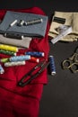 Sewing objects with vintage golden metal scissors, various needles, thimbles, red cloth, spools of colored threads, cloth,