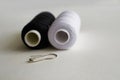 Sewing supplies. Two reels with black and white threads and a pin on a gray background Royalty Free Stock Photo