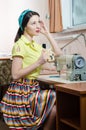 Sewing in workshop beautiful brunette young woman pinup girl with red lips and nails in yellow dress blue ribbon on her head Royalty Free Stock Photo