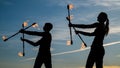 Sexi couple of guy and girl perform flaming baton twirling during fire performance in dark silhouettes on idyllic