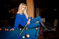 Sexual blonde lady posing on billiard table with the cue