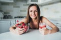 Sexual sports girl holding a bowl of strawberries and a glass of smoothie in the kitchen.
