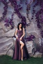 attractive lady with dark curled hair against stone wall with unusual magic plants, gorgeous charming countess in