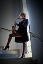 attractive woman with saxophone and long legs posing on stairs. Young attractive blonde playing sax. Musical instrument. Jazz Royalty Free Stock Photo