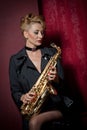 attractive woman with saxophone posing on red background. Young sensual blonde playing sax. Musical instrument, jazz Royalty Free Stock Photo