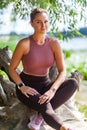 Sexy attractive woman in yoga pants and top sitting in forest taking rest after trainings, looking at camera