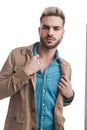 Sexy bearded casual man in denim shirt pulling and fixing jacket