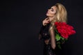 beautiful blond model in elegant dress holding a bouquet of red roses. Valentines`s gift on a black background Royalty Free Stock Photo