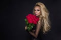 beautiful blond model in elegant dress holding a bouquet of red roses. Valentines`s gift on a black background Royalty Free Stock Photo