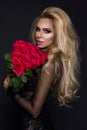 beautiful blond model in elegant dress holding a bouquet of red roses. Valentines`s gift on a black background Royalty Free Stock Photo
