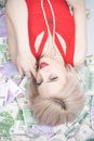 A beautiful blonde woman in a red dress is lying on a lot of money and enjoying life. rich caucasian girl top view