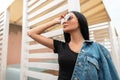 Sexy beautiful young hipster woman in a trendy denim jacket in a stylish black top in vintage sunglasses resting Royalty Free Stock Photo