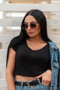 Sexy beautiful young hipster woman in a trendy denim skirt in a fashionable black top in a vintage jeans jacket in sunglasses Royalty Free Stock Photo