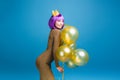 Sexy beautiful young woman in fashionable luxury dress having fun with golden balloons on blue background. Cut purple