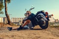 Sexy biker man wearing jeans and leather jacket sitting relaxed by his motorcycle Royalty Free Stock Photo