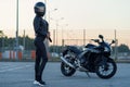 Sexy biker woman in black leather jacket and full face helmet stands near stylish sports motorcycle. Urban parking Royalty Free Stock Photo