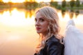 sexy blonde woman in black leather jacket and shorts with white angel wings. demon or angel in hell or heaven. sunset Royalty Free Stock Photo