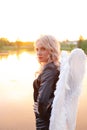 sexy blonde woman in black leather jacket and shorts with white angel wings. demon or angel in hell or heaven. sunset Royalty Free Stock Photo