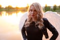 sexy blonde woman in black leather jacket and shorts with white angel wings. demon or angel in hell or heaven. sunset Royalty Free Stock Photo