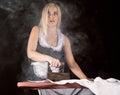 blonde woman in housekeeper suit, ironing white shirt with old iron. retro style on a dark background Royalty Free Stock Photo