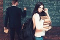 Sexy brunette female student holding her glasses while carrying pile of books. Young college girl in pink cardigan Royalty Free Stock Photo