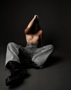 Sexy brunette woman wearing pearl necklace, bra, wide jeans and massive boots sits on floor hiding her face looking Royalty Free Stock Photo