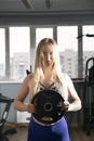 Sexy caucasian fitness model posing in the gym. Blonde girl is holding dumbbells. Sport, healthy lifestyle. Vertical frame Royalty Free Stock Photo