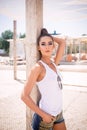 Sexy Caucasian Woman on the Beach With White Undershirt, Jeans Shorts, Sunglasses and Pony Tail, Leaning on a Wooden Pole, Looking Royalty Free Stock Photo