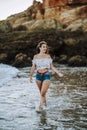 Sexy caucasian woman in short jeans and an open shirt showing a fit belly walking along a coastline Royalty Free Stock Photo