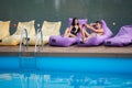 couple relaxing with drinks on cushioned loungers by swimming pool and river on the background