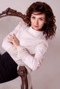 Sexy curly brunette leaned on a beautiful vintage armchair. Business elegant girl in a blouse and a skirt sits on a chair, busines