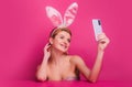 Sexy easter bunny woman with rabbit ears having call holding smart phone in hand shooting selfie on front camera Royalty Free Stock Photo